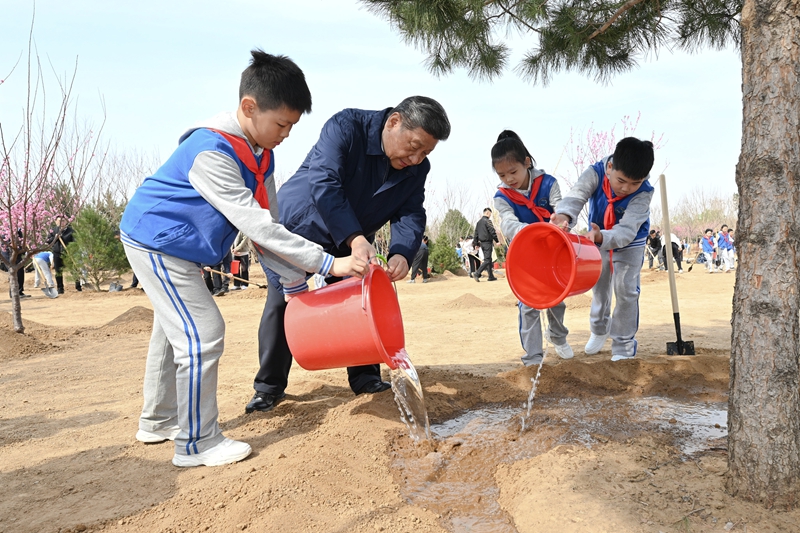 4月3日，党和国家领导人习近平、李强、赵乐际、王沪宁、蔡奇、丁薛祥、李希、韩正等来到北京市丰台区永定河畔参加首都义务植树活动。这是习近平同少先队员一起给刚栽下的树苗浇水。